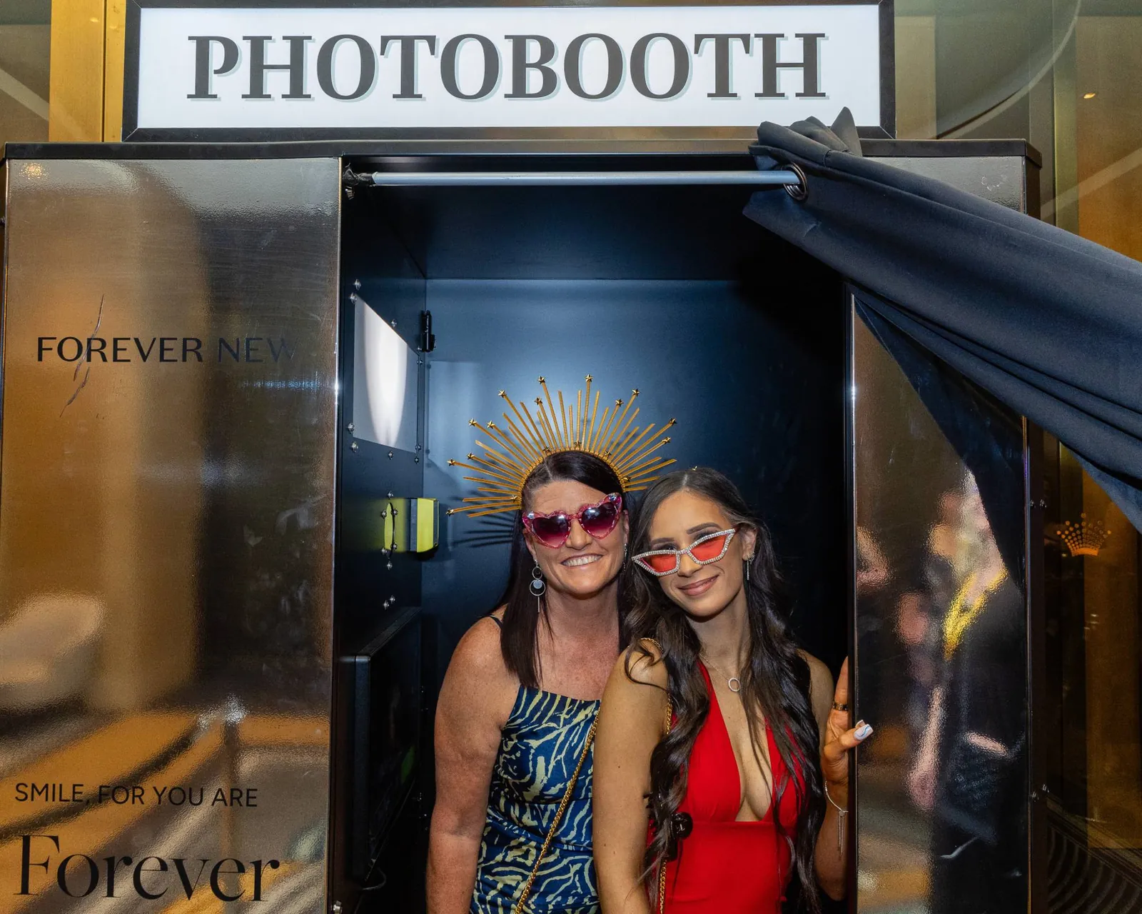 Two guests in party sunglasses inside a Forever New-branded photo booth