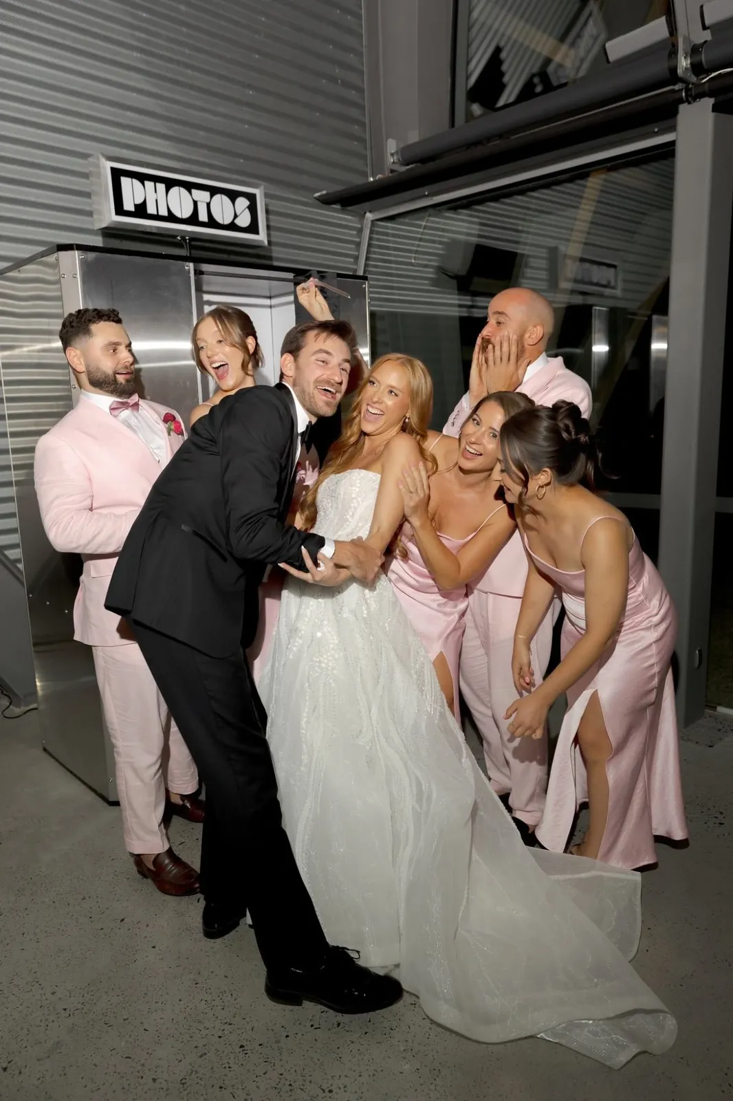 A bride, groom and wedding party laughing in front of a photo booth